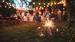 © Khawla - A brightly lit sparkler in the foreground, casting a warm glow, with a festive backyard party in the background. 4th july, memorial. independence