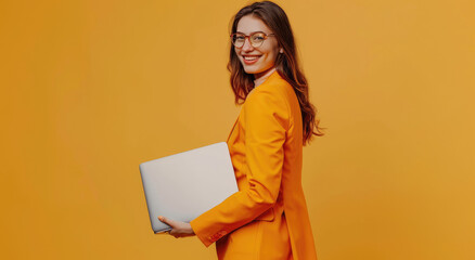 Wall Mural - A happy woman in an orange suit holds and shows a laptop computer isolated on a beige background