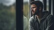 © BURINKUL - A thoughtful man looking out the window on a rainy day, deep in contemplation and reflection, capturing a sense of melancholy and introspection.