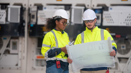 Wall Mural - Engineers railway survey wearing safety uniform and helmet under conversation blueprint on hand inspect checking cargo containers railway work on railroad station is transportation industry concept.