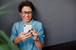 © peopleimages.com - Hands, smartphone and happy woman by plant for funny text, meme or update on social media. Scrolling, cellphone and female influencer with glasses for joke, comedy and humor story on online platform