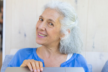 Wall Mural - At home, Caucasian senior woman in blue, smiling, hands on laptop during video call