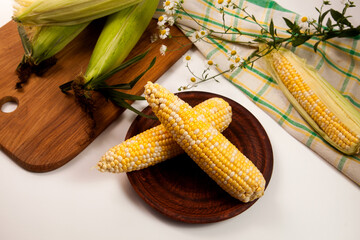 Wall Mural - Clay plate with two cobs sweet corn on white wooden background..