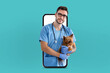 © Prostock-studio - A veterinarian wearing blue scrubs and gloves is holding a Yorkshire Terrier while appearing to come out of a smartphone screen. The scene symbolizes a virtual pet consultation