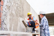 © Robert Kneschke - Senior male builder gesturing while talking to female mason plastering wall at construction site