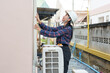 © Ekkasit A Siam - Asian female home inspector in safety helmet examining exterior wall near air conditioning unit. Represents meticulous inspection process ensuring all aspects meet quality before handing over to owner