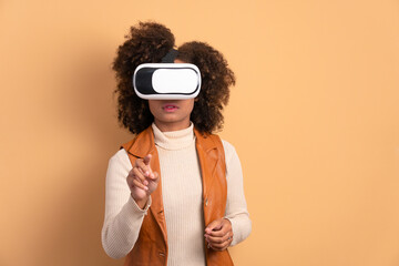 Wall Mural - excited black young woman Using VR headset and gesturing in beige background. virtual reality, technology simulation concept.