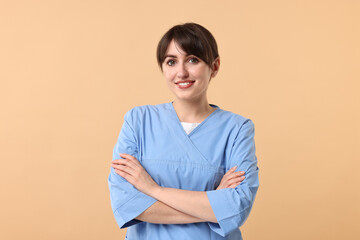 Wall Mural - Portrait of smiling medical assistant with crossed arms on beige background