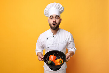 Canvas Print - Surprised chef holding colander with vegetables on yellow background