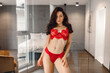 © Nataliya - Pretty young lady standing in a spacious apartment room near the big glass door while posing in sexy red lingerie. Lifestyle concept