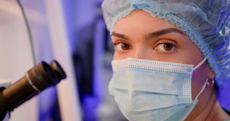 Portrait of research student scientist. An embryologist wearing a mask and hair net works in a laboratory, performing artificial fertilization of a human egg using a microscope for IVF procedures.