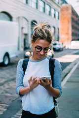 Wall Mural - Young woman with smartphone using application for calling taxi online walking on city street,hipster girl satisfied with internet connection sending photos to friend via mobile phone while strolling