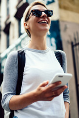 Wall Mural - smiling hipster girl in sunglasses strolling in downtown using mobile phone application for navigate