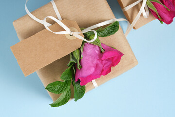 Wall Mural - Fragment of brown gift box with blank gifttag and rosehip flowers on blue background. Space for your text