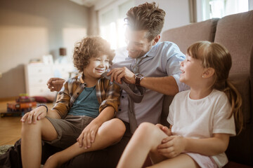 Wall Mural - Happy father playing with son and daughter at home