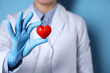 © New Africa - Doctor wearing medical gloves holding decorative heart on light blue background, closeup