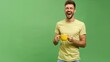 © Abubakar - Male in t-shirt and jeans laughing while holding a yellow coffee cup against a solid green background, perfect for a joyful and minimalist stock image