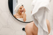© Nataliya - Happy beautiful lady having fun and removing makeup with cotton pad, standing in the bathroom, looking at the mirror. Beauty treatment, face skin care concept