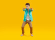 © Studio Romantic - Cheerful funny guy jokingly pretending to squat with arms outstretched, isolated on orange background. Young Caucasian man in casual shirt, t-shirt and pants is fooling around and smiling. Full length