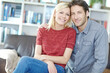 © Grady Reese/peopleimages.com - Couple, portrait and hug on sofa in home living room, bonding or relaxing and having fun. Smile, man and woman sitting on couch for embrace, happiness and enjoying security together for support