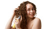 © master1305 - Young woman with curly brown hair using hair treatment spray for glossy shiny look isolated on white background. Concept of natural beauty, skincare, wellness, cosmetology, cosmetics