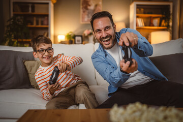 Adult caucasian father and son play video games with joystick at home