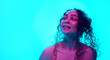 © master1305 - Happy, smiling, young woman with curly hair posing against cyan background in neon light. Spotless, well-kept skin. Concept of beauty, wellness, self-care, fashion, cosmetics