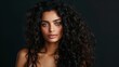 © MD Media - A beautiful woman with long curly hair posing for the camera, showcasing her shiny and healthy hair against a dark salon background.Beauty brunette girl with wavy black hair .