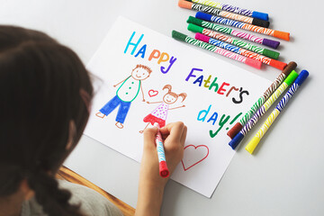 girl daughter draws a card to dad for Father's Day, drawing of dad and daughter on a white sheet with multi-colored felt-tip pens, concept of sweet wishes