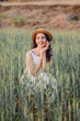 © Satori Studio - A woman is sitting in a field of tall grass, wearing a straw hat and a white dress. She is smiling and she is enjoying the outdoors