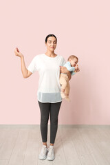 Wall Mural - Beautiful young sporty woman with her little baby meditating near pink wall