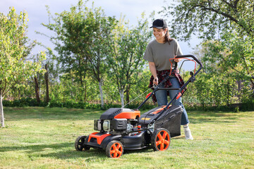 Wall Mural - Smiling woman cutting green grass with lawn mower in garden