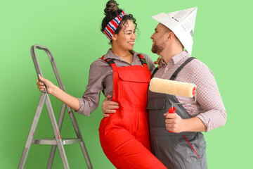 Poster - Beautiful young happy couple with paint roller near green wall doing repair in new house