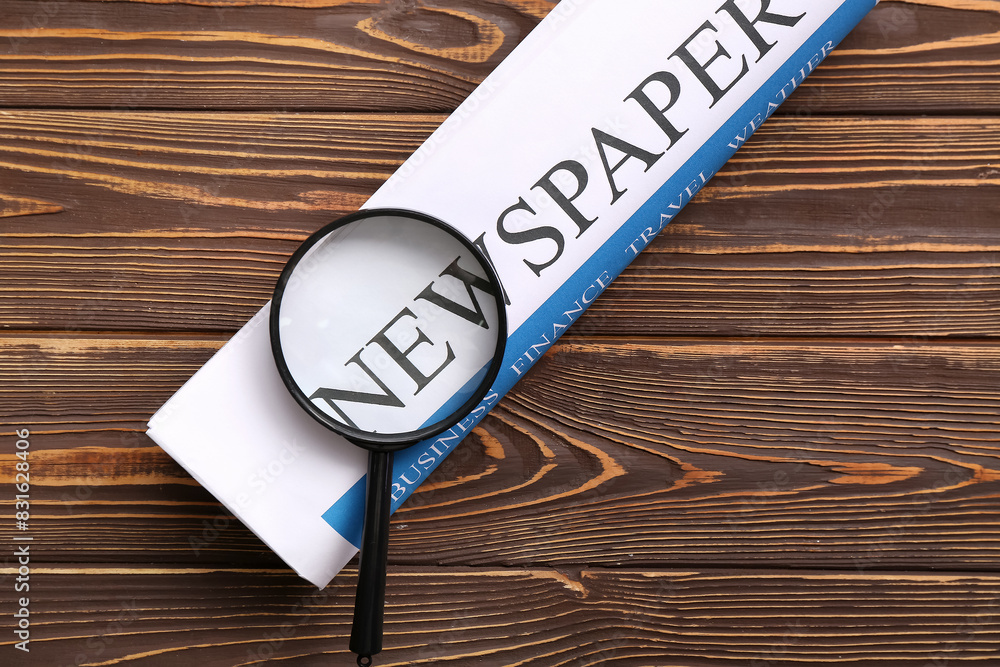 Newspaper with magnifying glass on wooden background