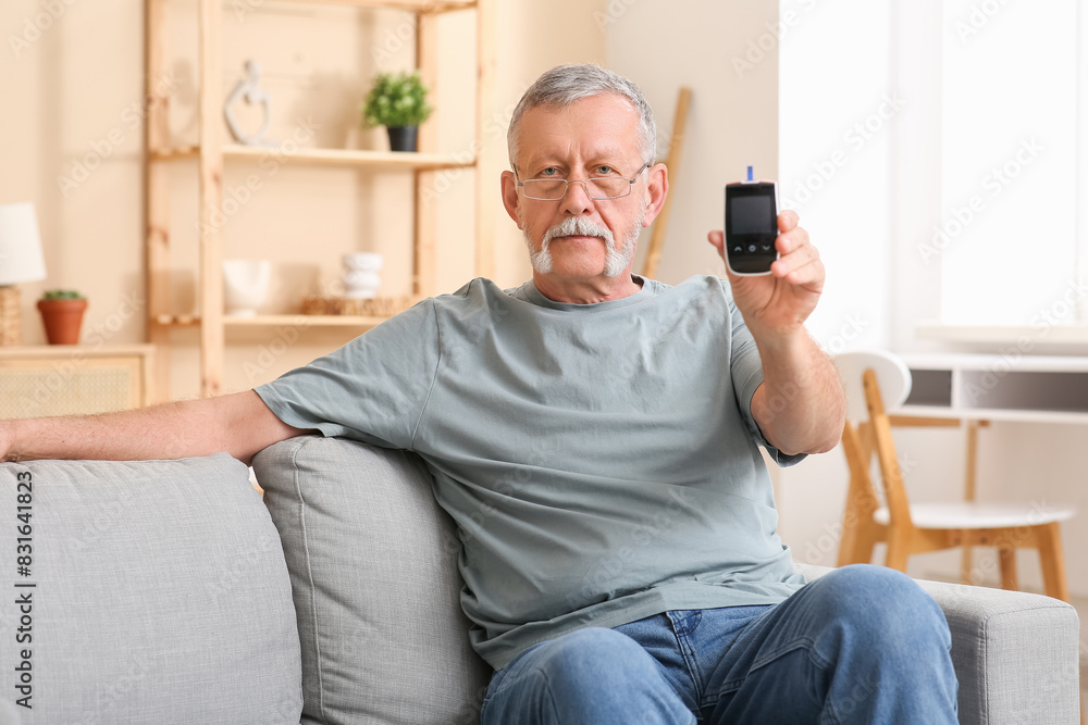 Senior man with glucometer sitting on sofa at home. Diabetes concept
