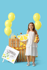 Wall Mural - Cute little girl with lemons near lemonade stand on blue background