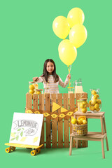 Canvas Print - Cute little Asian girl with balloons at lemonade stand on green background