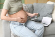 © Pixel-Shot - Pregnant young woman with calculator sitting on sofa in living room