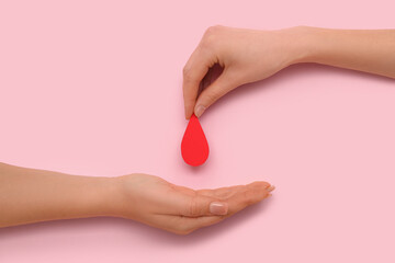 Wall Mural - Female hands with red paper drop on red background. Donation blood concept.