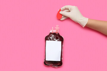 Wall Mural - Female hand holding paper blood drop and blood pack for transfusion on pink background. World blood donor day.
