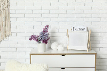 Canvas Print - Interior of living room with bouquet of lilacs branches on chest of drawers near white brick wall