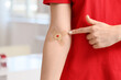 © Pixel-Shot - Female blood donor pointing at applied patch in clinic, closeup