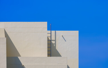 Wall Mural - Geometric yellow office building with ladder on rooftop against blue clear sky background in minimal style, modern exterior architecture backdrop design