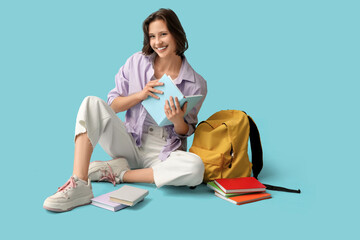 Wall Mural - Beautiful female student with backpack and books sitting on blue background