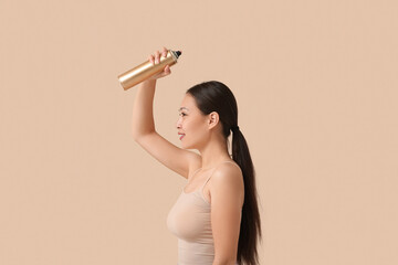 Poster - Beautiful young happy woman applying hair spray on beige background