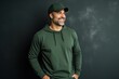 © Stocknterias - Happy man in green hoodie and cap standing against dark background.