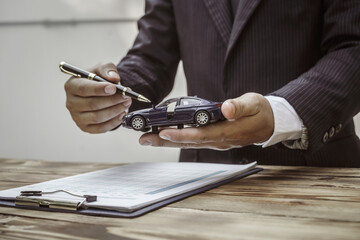 A businessman in a formal suit signs a contract, hands close up, highlighting financial terms like amortization, APR, and asset management, documents symbolizing various loan and insurance concepts.