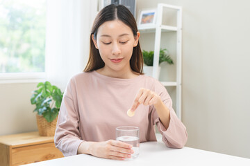 Smile asian young woman putting or dropping effervescent tablet into glass of water, holding pain pill, painkiller medicine, aspirin for treatment, take vitamin c for hangover. Health care concept.