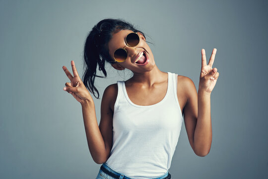 Studio, woman and funny with peace sign, confidence and trendy accessory as sunglasses. Indian female model, hand gesture and scream with emoji reaction, v symbol and stylish girl by gray background