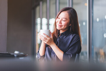 Wall Mural - Portrait image of a beautiful young asian woman holding and drinking hot coffee in cafe